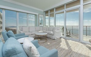 Ein geräumiger Balkon mit Blick auf den Strand, ein hellblaues Sofa und ein runder Couchtisch.