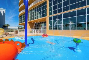 Ein Wassererlebnisbereich mit Pool, einer blauen Säule und einem Gebäude mit großen Fenstern im Hintergrund.