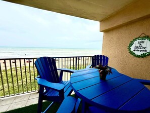 Un balcón con dos sillas azules y una mesa, con vista a la playa.