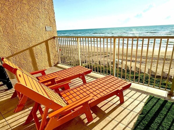 Een balkon met uitzicht op het strand, voorzien van houten meubilair.