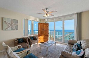 A living room with a ceiling fan, a wooden cabinet, a sofa, and a view of the ocean through large glass doors. - Inn at Summerwind 1101 | Beachfront Corner Condo | Outdoor Pool | Fitness Center | My Beach Getaways (Navarre)