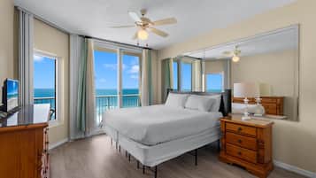 A hotel room with a bed, a dresser, a television, and a large window offering a view of the ocean.