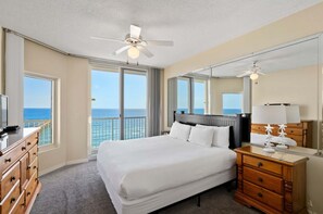 A hotel room with a bed, a dresser, a mirror, a ceiling fan, and a view of the ocean. - Inn at Summerwind 1101 | Beachfront Corner Condo | Outdoor Pool | Fitness Center | My Beach Getaways (Navarre)