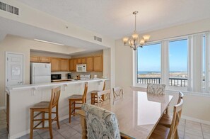 Una cocina con armarios de madera, un refrigerador blanco, un microondas y un comedor con mesa y sillas de vidrio.
