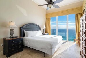 Ein Schlafzimmer mit Bett, Nachttisch, Lampe, Kommode und Blick aufs Meer.