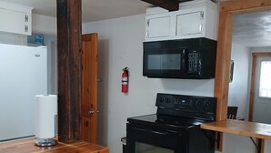 A compact kitchen with a microwave, stove, and white cabinets. - Cottage with kitchen, walking distance to airport, restaurants, historical sites (Idaho City)