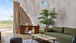 Ein Zeltraum mit einem grünen Sofa, einem Holztisch, einem Stuhl, einer Topfpflanze und einer Uhr an der Wand.