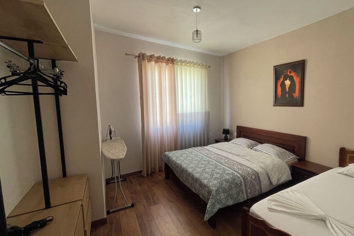 Un dormitorio con cama, mesita de noche, perchero, lámpara de pie y un cuadro en la pared.