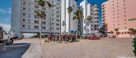 A multi-story hotel with a central courtyard, palm trees, and a parking area.