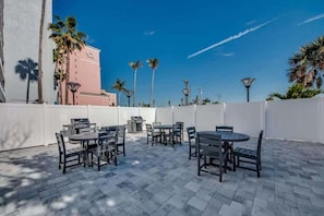 Une terrasse extérieure dotée de plusieurs tables et chaises, d’un barbecue et de palmiers.
