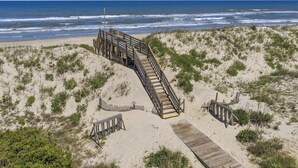 Una escalera de madera que baja hacia una playa arenosa con vista al océano.