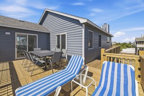 Een terras met een tafel en stoelen, een klein huisje met een raam, en een houten hek.