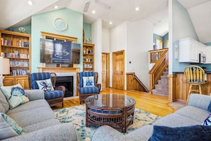 A spacious living room with a fireplace, bookshelves, a television, and a staircase leading to another level. - Salty Crab | 1,200 ft to the beach | Private Pool, Hot Tub, Dog Friendly, and Community Pool (Corolla)