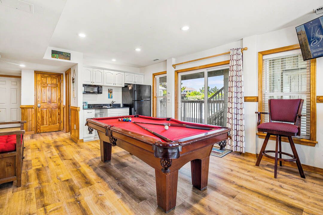 A pool table in a room with a kitchen, a dining area, and a view of a balcony.