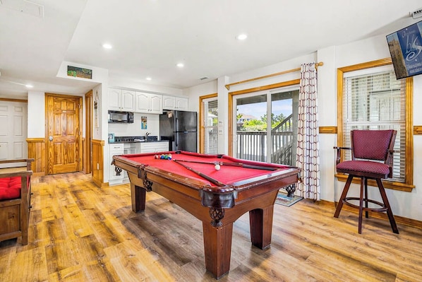 A pool table in a room with a kitchen, a dining area, and a view of a balcony. - Salty Crab | 1,200 ft to the beach | Private Pool, Hot Tub, Dog Friendly, and Community Pool (Corolla)