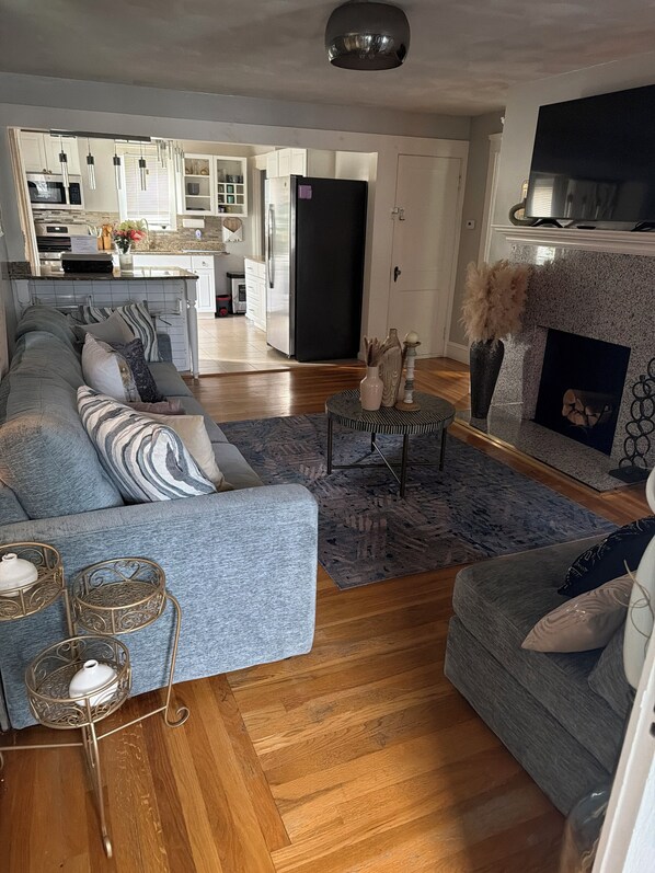 A modern living room with a sectional sofa, a fireplace, and a kitchen in the background. - The Power House Retreat Near Providence & Brown (Pawtucket)