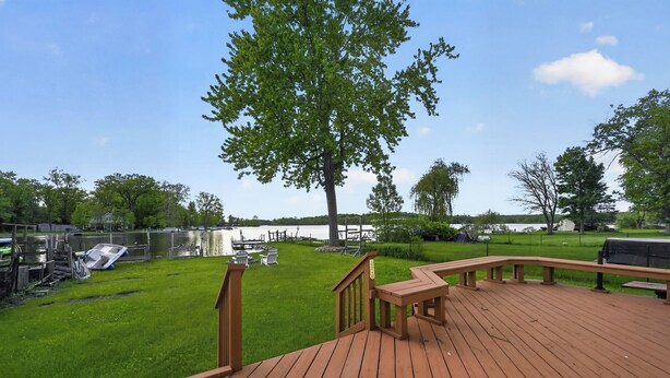Une terrasse en bois avec une table de pique-nique, un grand arbre et une zone herbeuse avec un quai pour bateaux.
