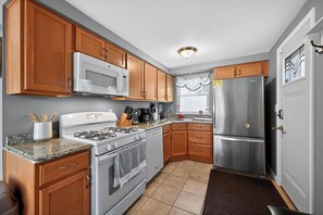 Una cocina con armarios de madera, un refrigerador de acero inoxidable, un microondas, una estufa y un lavamanos.
