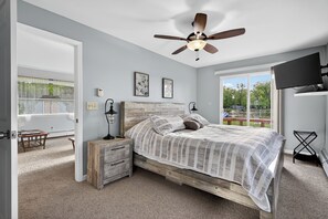Un dormitorio con cama de madera, ventilador de techo, televisor y vistas al exterior.