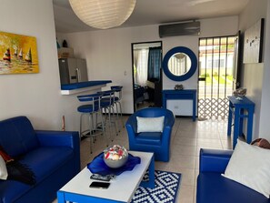 A living room with blue furniture, a dining area with a bar, a kitchen, and a view through a glass door. - House with Private Pool in Playa Bejuco (Parrita)