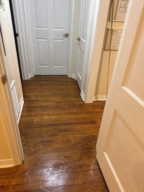 A hallway with wooden flooring, white doors, and a vent on the left wall.