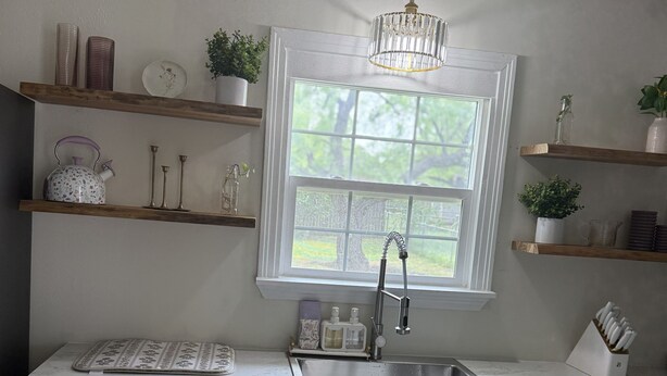 A kitchen with a window, a sink, and wooden shelves with various items.