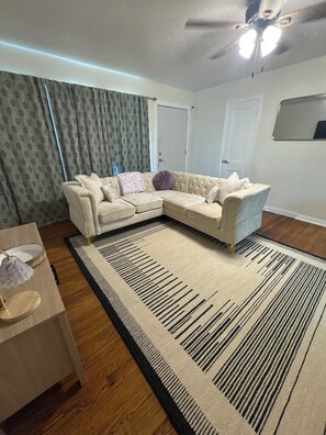 A living room with a sectional sofa, a wooden coffee table, a patterned rug, and a ceiling fan.