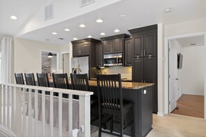 A modern kitchen with dark cabinetry, a central island, and a dining area with chairs.