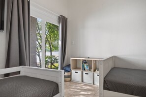 A room with two beds, a window with curtains, a small seating area, and storage units.