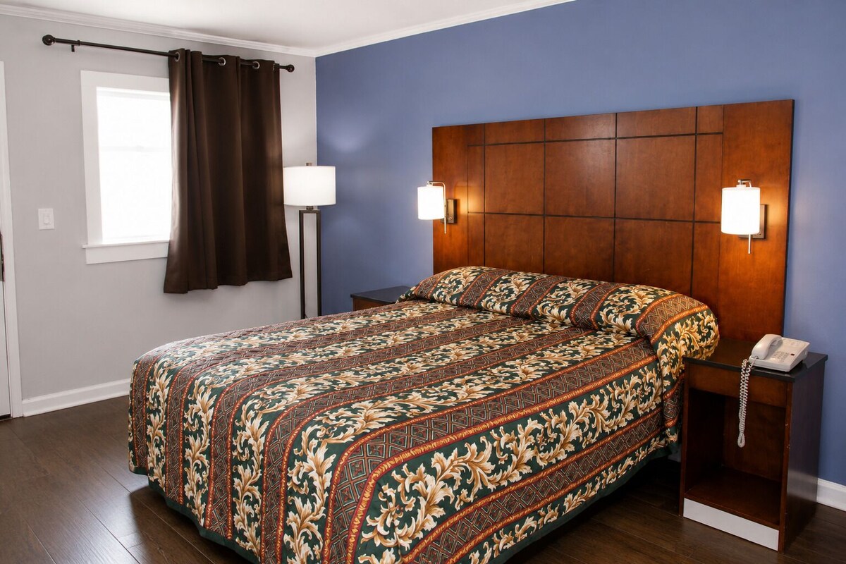A bedroom with a large bed, two bedside lamps, a telephone, and a window with curtains.