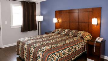 A bedroom with a large bed, two bedside lamps, a telephone, and a window with curtains.