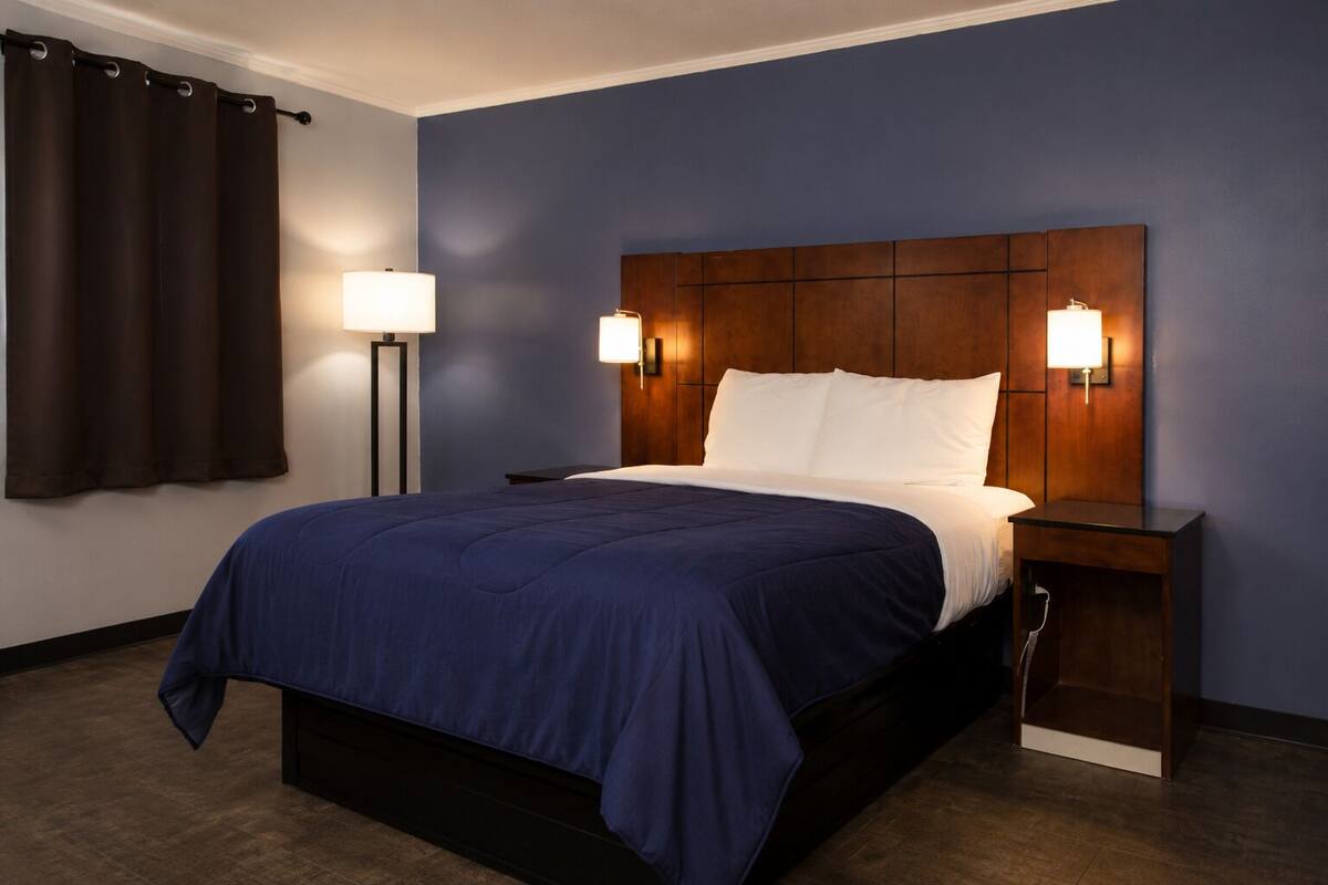 A hotel room with a large bed, two bedside lamps, a dark blue wall, and a wooden headboard.