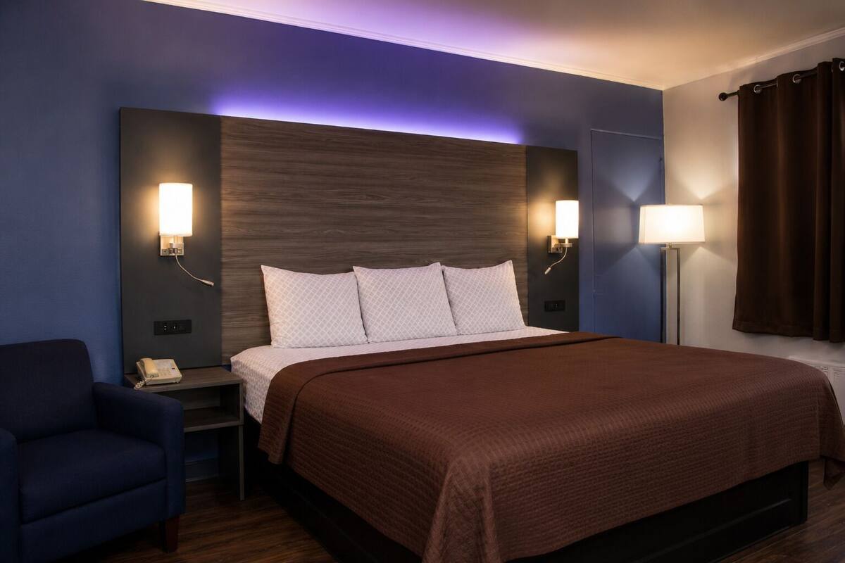 A hotel room with a bed, bedside lamps, a phone, a chair, and a nightstand.
