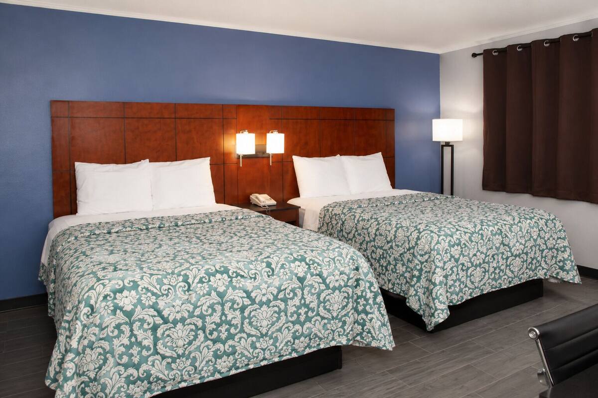 A hotel room with two beds, a wooden headboard, a nightstand with a phone, and a lamp.