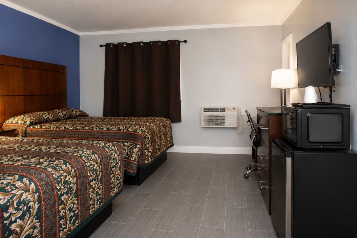 A hotel room with two beds, a desk with a computer, a television, and an air conditioning unit.