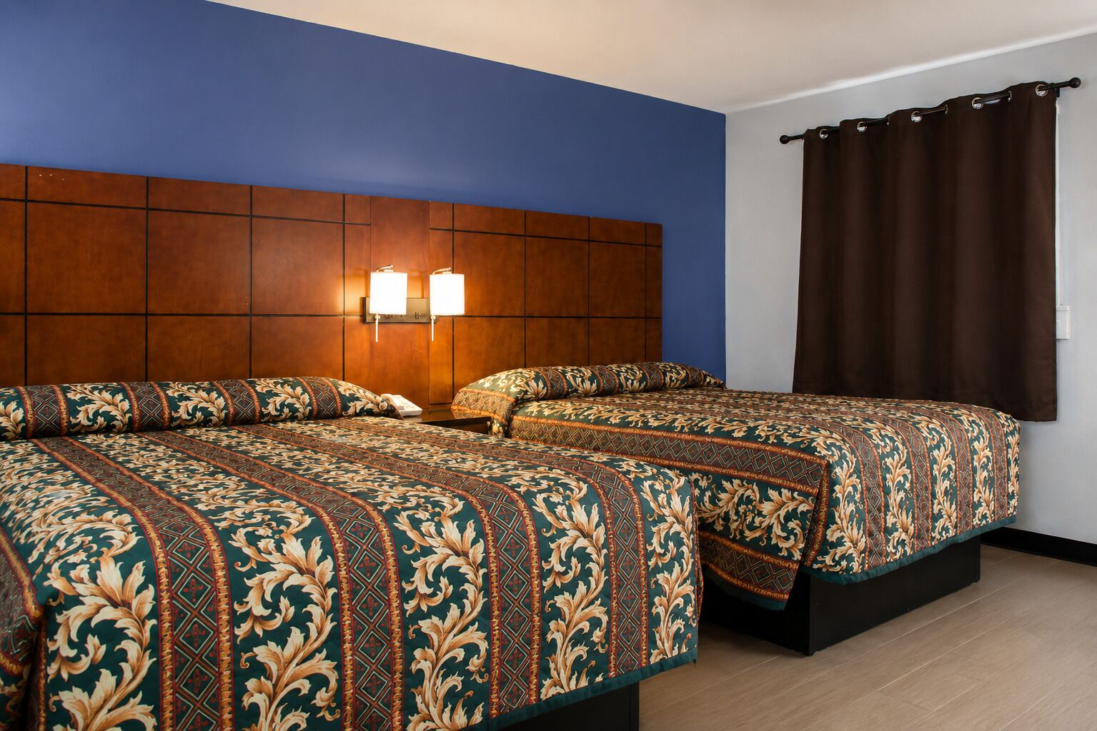 A double bed room with a wooden headboard, two bedside lamps, and a brown curtain.