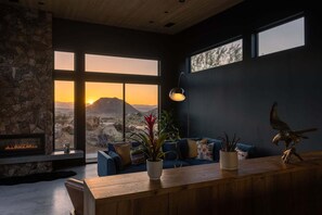 Una sala de estar moderna con pared de piedra, chimenea, ventana grande con vistas a un paisaje desértico y sofá azul con cojines decorativos.