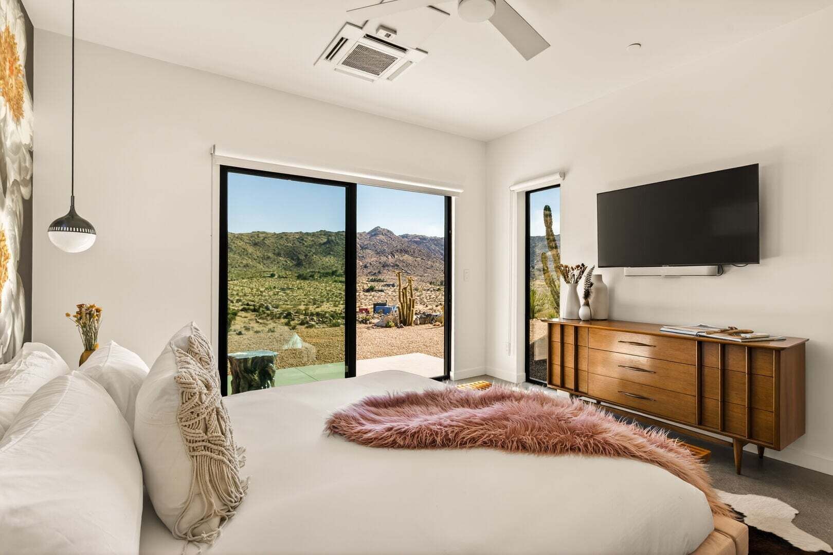 Ein Schlafzimmer mit einem großen Bett, einem Flachbildfernseher, einer hölzernen Kommode und einer Glasschiebetür mit Blick auf die Wüste.