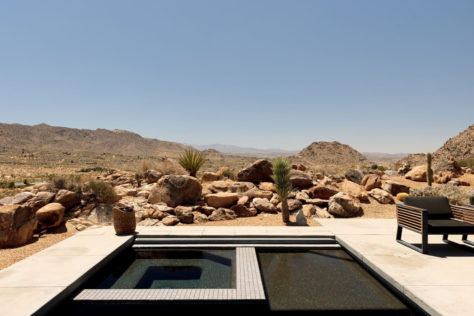A pool area with large rocks and a cactus, surrounded by desert landscape.