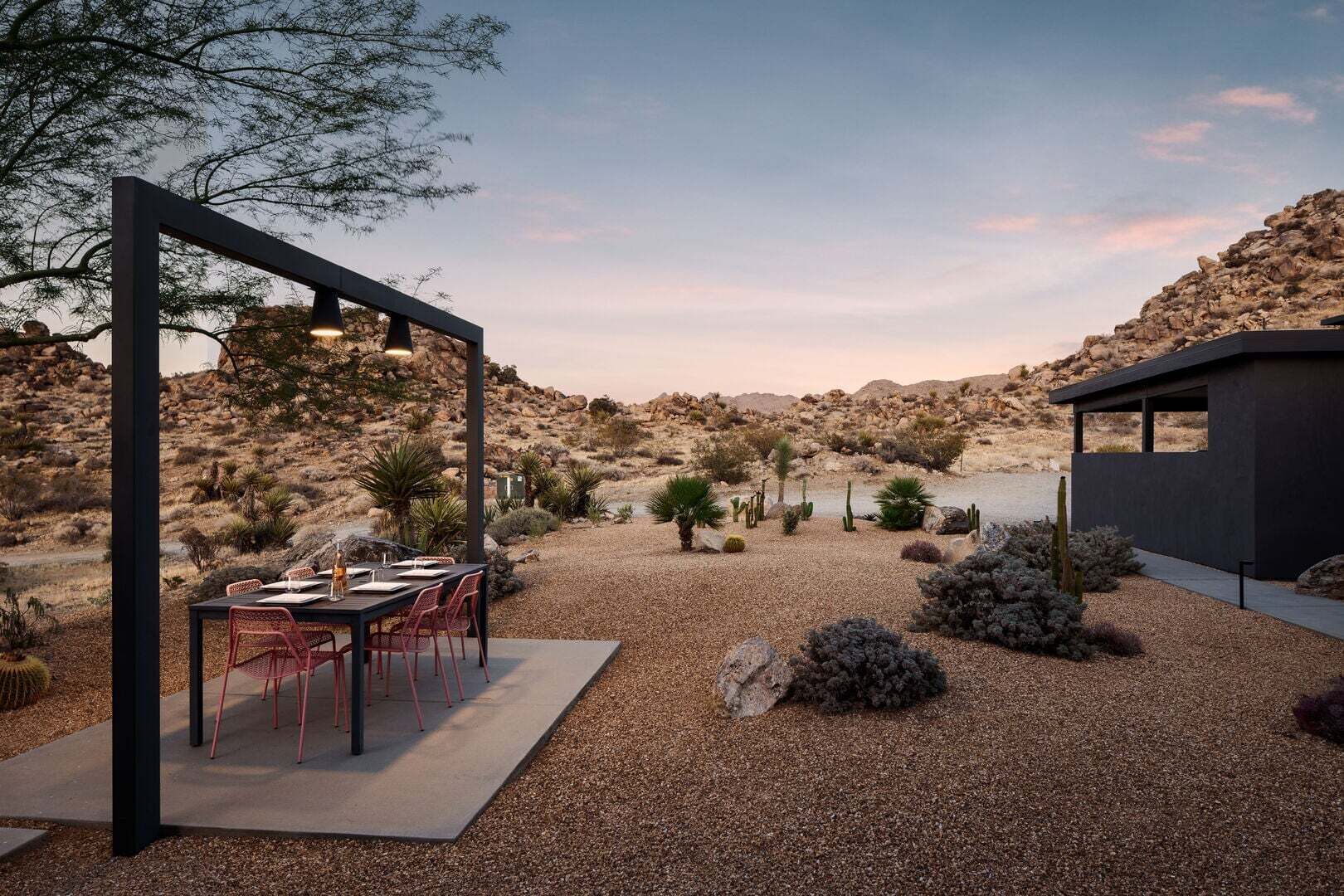 An outdoor dining area with a table and chairs, surrounded by desert vegetation and a view of a lake.