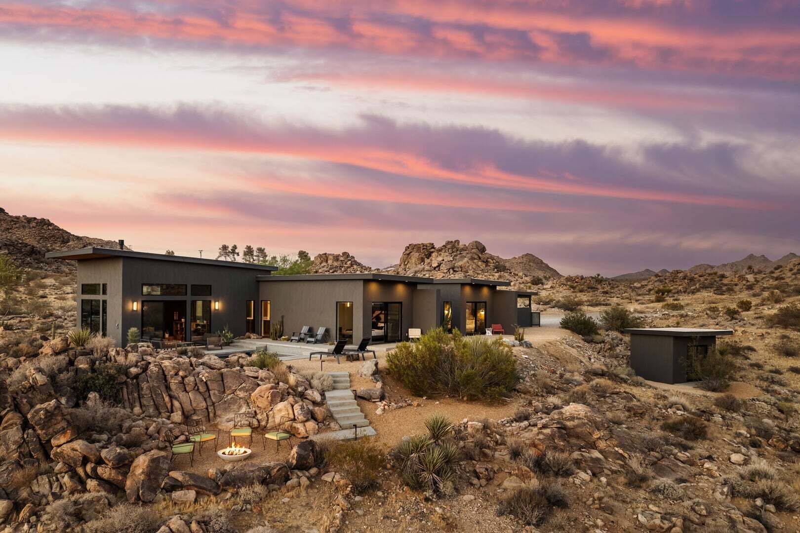 A modern two-story house with a patio area, surrounded by desert landscape.