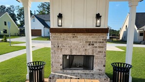 An outdoor patio with a stone fireplace, two trash bins, and a wooden table. - Pet-Friendly 4BR 5 Min to LakePoint with TV Room (Emerson)