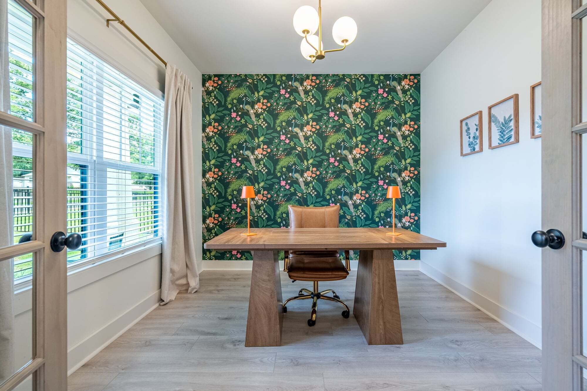 Una stanza con un tavolo di legno, una sedia da ufficio, carta da parati decorata e un lampadario.