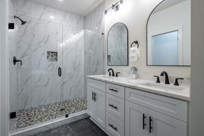 A modern bathroom with a shower, a glass-enclosed walk-in shower, a vanity with a mirror, and a tiled floor.