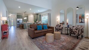 A spacious living area with a brown leather sofa, two patterned armchairs, a woven rug, and a kitchen in the background. - Pet-Friendly 4BR 5 Min to LakePoint with TV Room (Emerson)