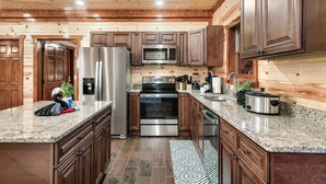 A kitchen with wooden cabinets, stainless steel appliances, granite countertops, and a herringbone-patterned rug. - 8 En-Suite | Sleeps 28 | Indoor Pool | Hot Tub | Mini Golf (Sevierville)