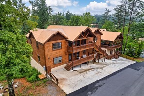 A large log cabin with multiple levels and a balcony, surrounded by lush greenery and a clear sky. - 8 En-Suite | Sleeps 28 | Indoor Pool | Hot Tub | Mini Golf (Sevierville)