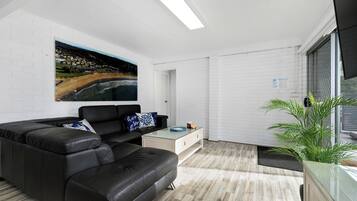 A modern living room with a black leather sofa, a glass coffee table, and a large painting on the wall.