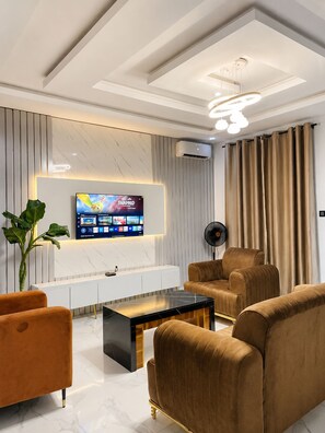 Una sala de estar moderna con un televisor de pantalla plana montado en la pared, una mesa consola blanca, una mesa de centro negra y dos sofás marrones.