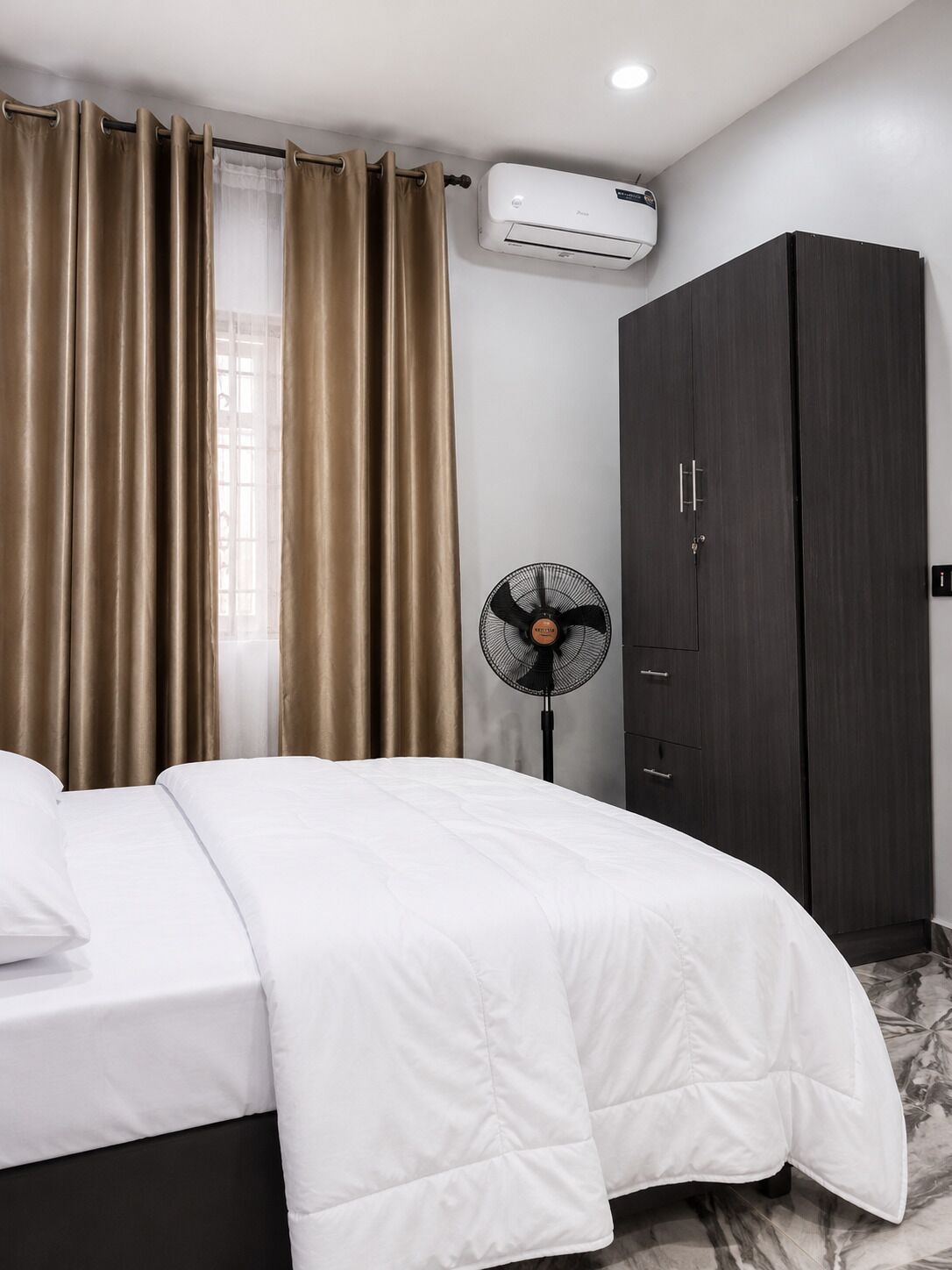 A bedroom with a bed, an air conditioning unit, a fan, and a wardrobe.